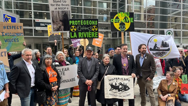 People pose for a photo holding colourful flags and signs outside a glassy court building.