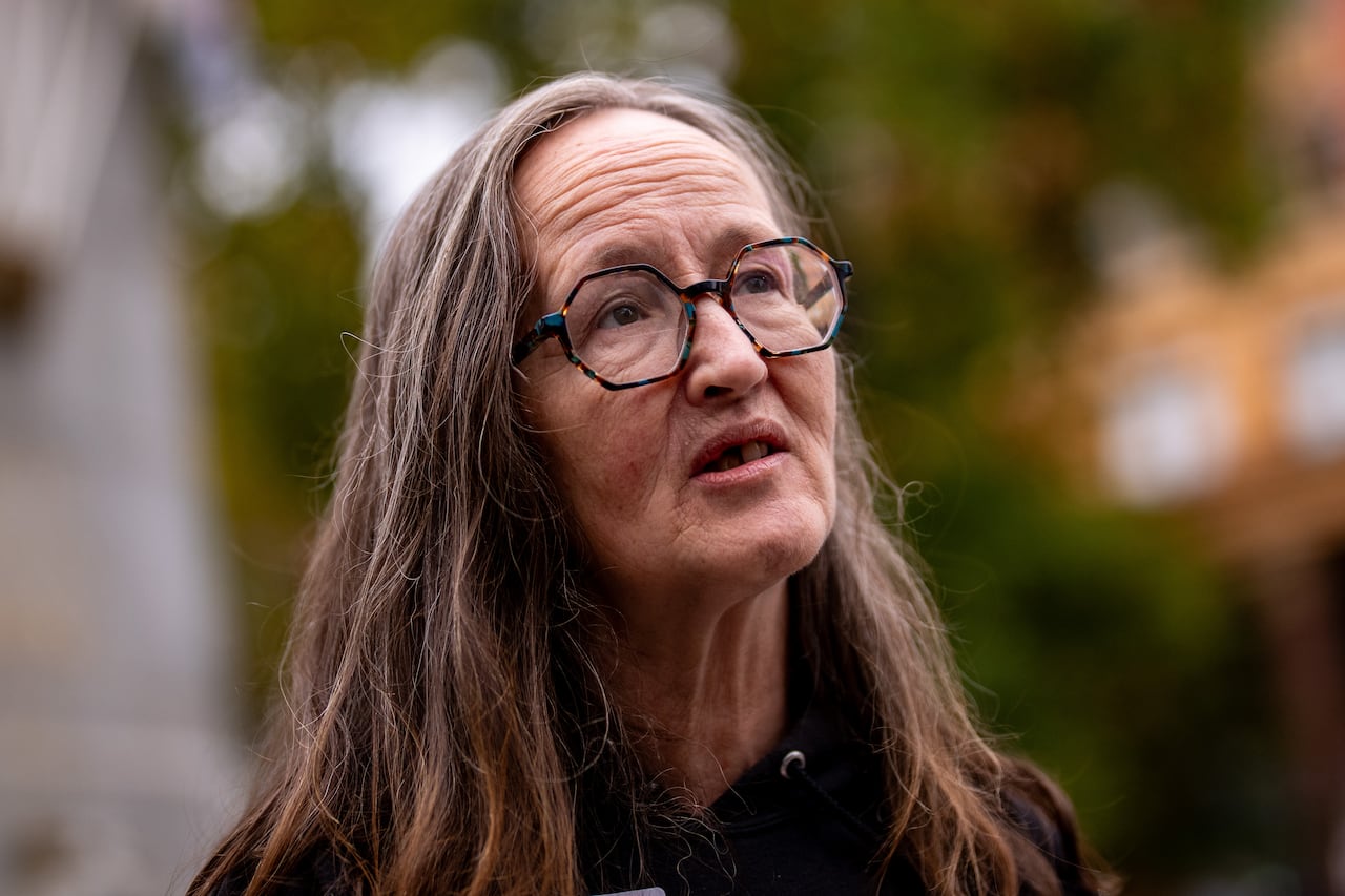 A woman with brown and grey hair wears hexagonal-shaped glasses.