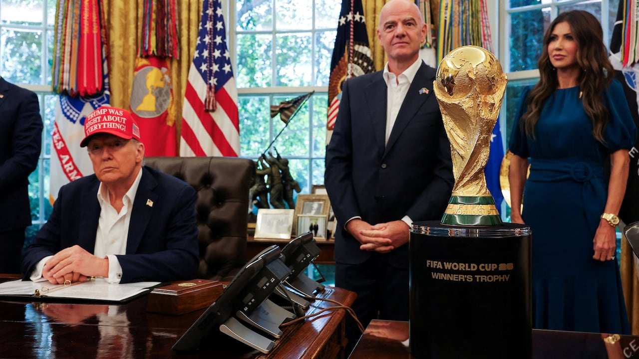 A man sits at a fancy desk wearing a red hat