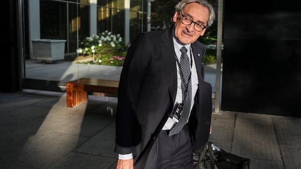 A man in a suit walks outside carrying a briefcase. 