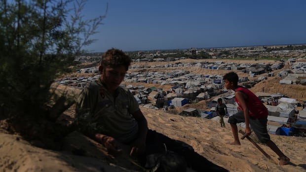 Two boys are seen in the foreground of a desert with rows of tents in the background