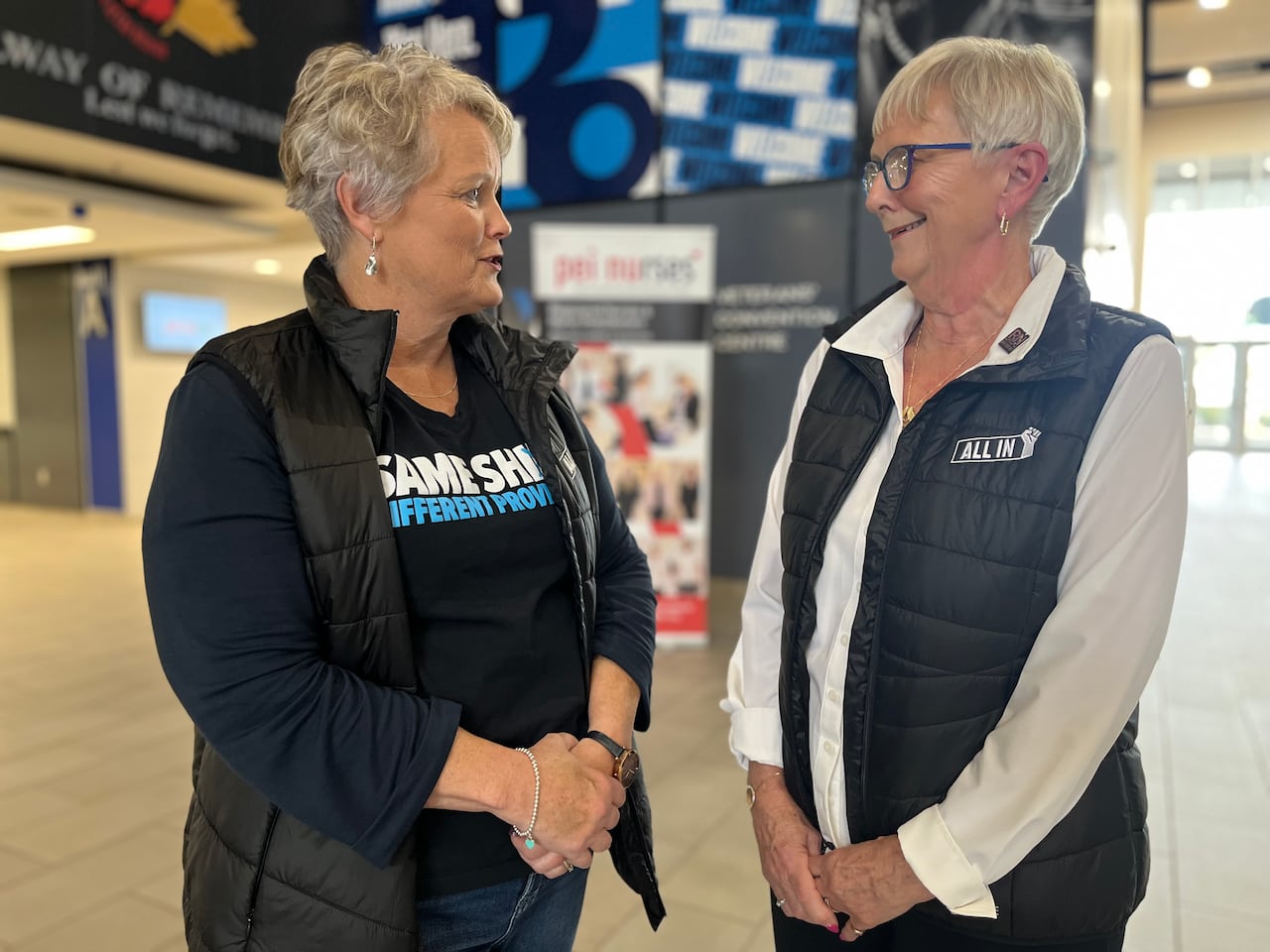 Two woman stand in the lobby of a large building speaking to each other.