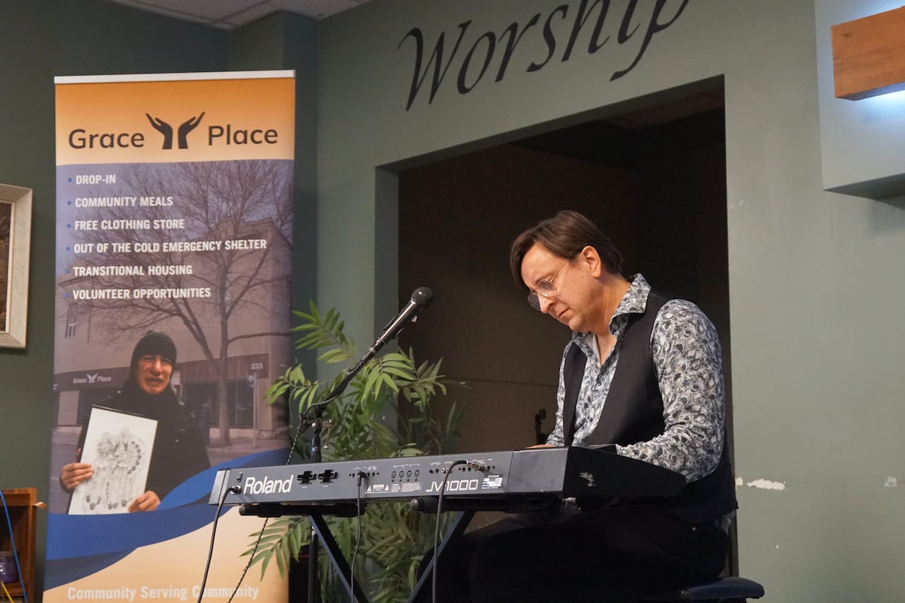 A person is seen playing the keyboard on a small stage indoors.