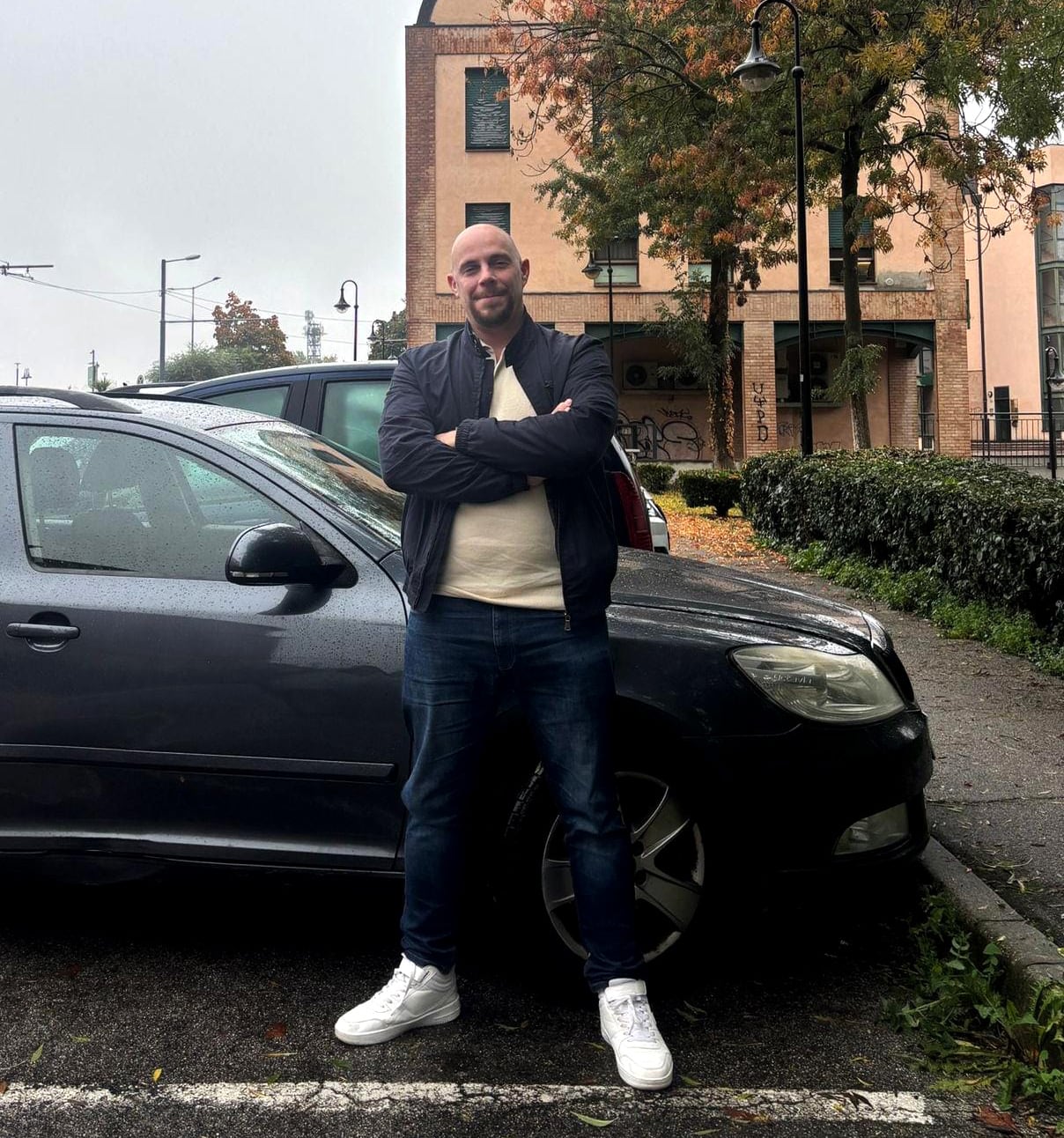 A man with white sneakers leaning against a black car.