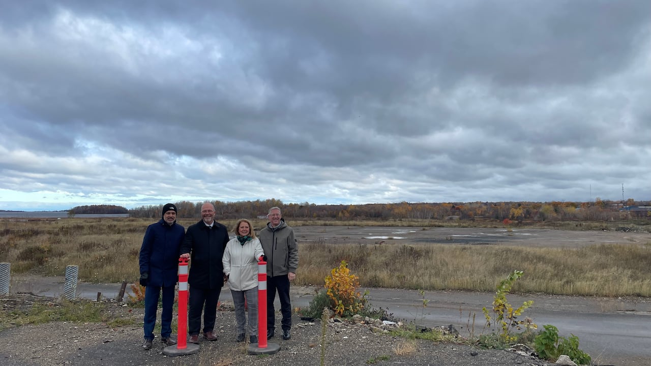 Four people stand together smiling in front of a vacant lot.