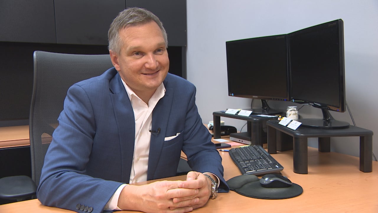 Man sitting at computer desk with short grey hair and a blue suit.