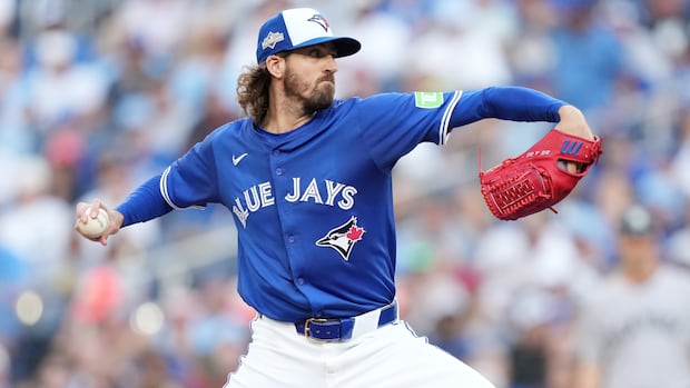 A male baseball pitcher winds up to throw the ball with his right hand.
