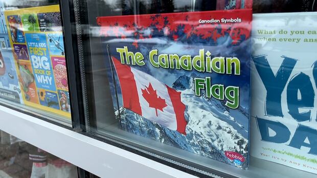 A book about the Canadian flag sits in the window of second-hand store Boomerang Kids. a book called The Canadian Flag with the maple leaf flag in front of a mountain sits in a large display window