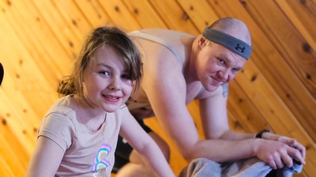 A young girl and an adult man ride stationary bikes side by side.