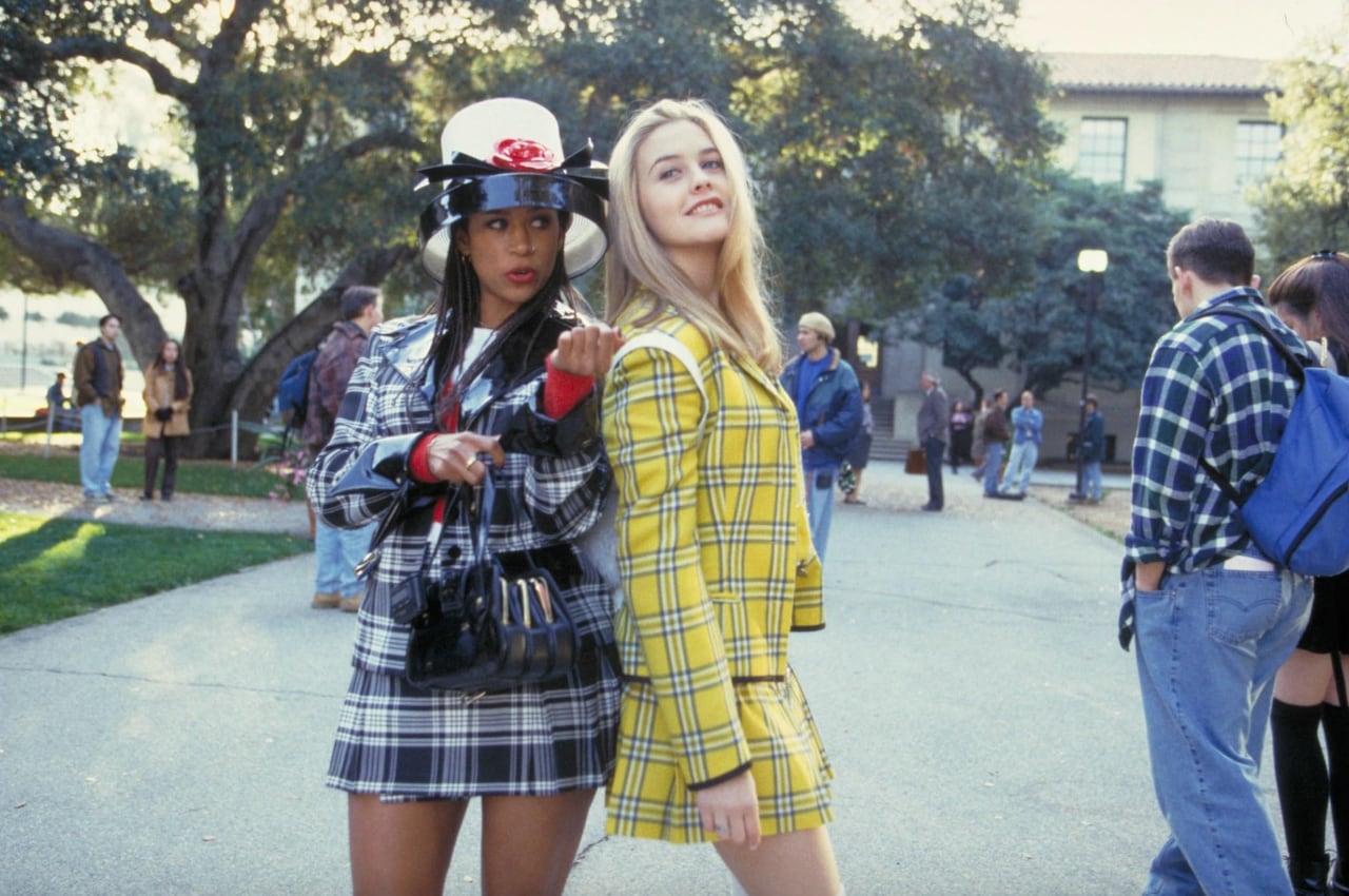 Two women in plaid skirt suits stand next to one another, outside on their school's campus. 