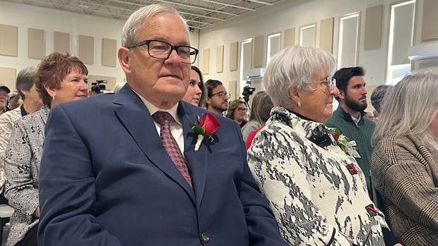 Lawrence MacAulay is not seeking re-election in the riding of Cardigan after representing eastern Prince Edward Island for more than 36 years in the House of Commons. Older man in navy business suit, with red rose on his lapel, sits in a community hall among a crowd of dozens of people.