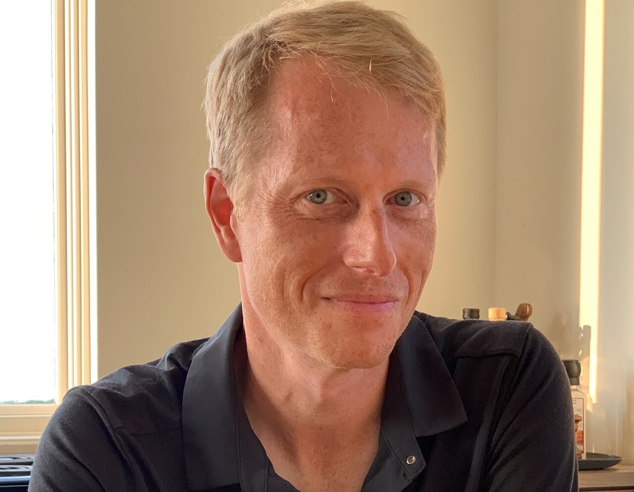 A headshot of a smiling man weating a black polo shirt.