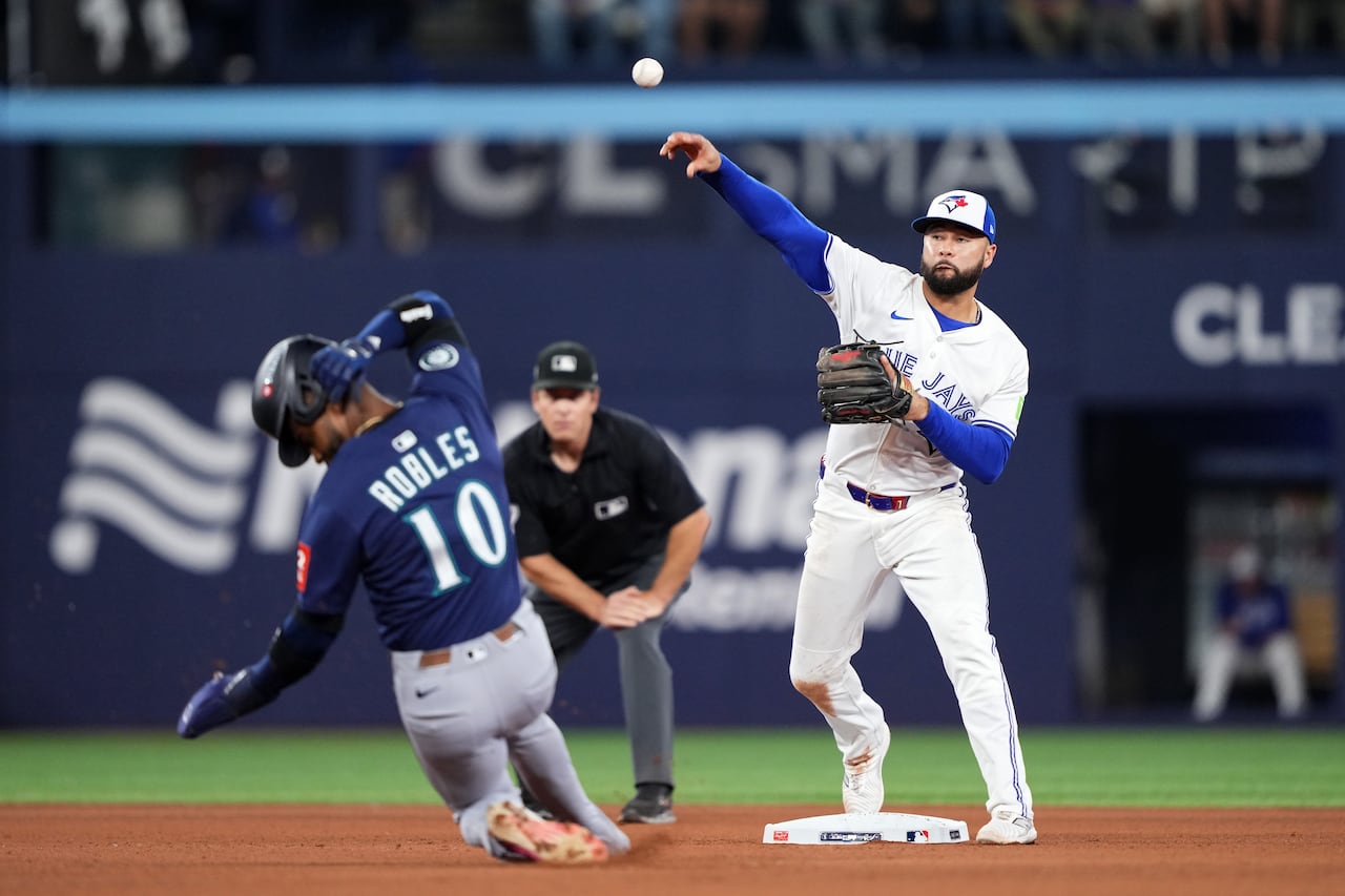 A baseball player slides into a base, while a player on the opposing team throws a baseball past him