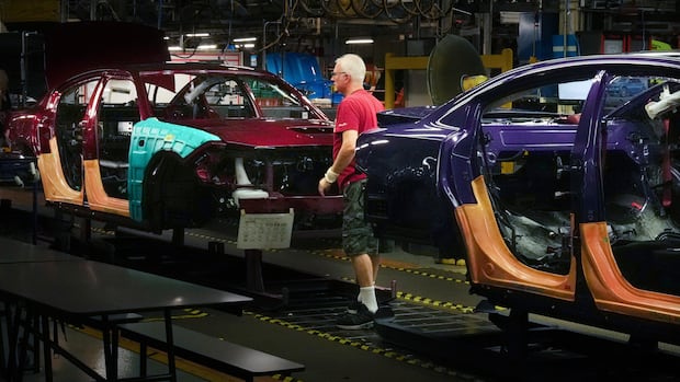 A man works on a vehicle assembly line in a large plant.