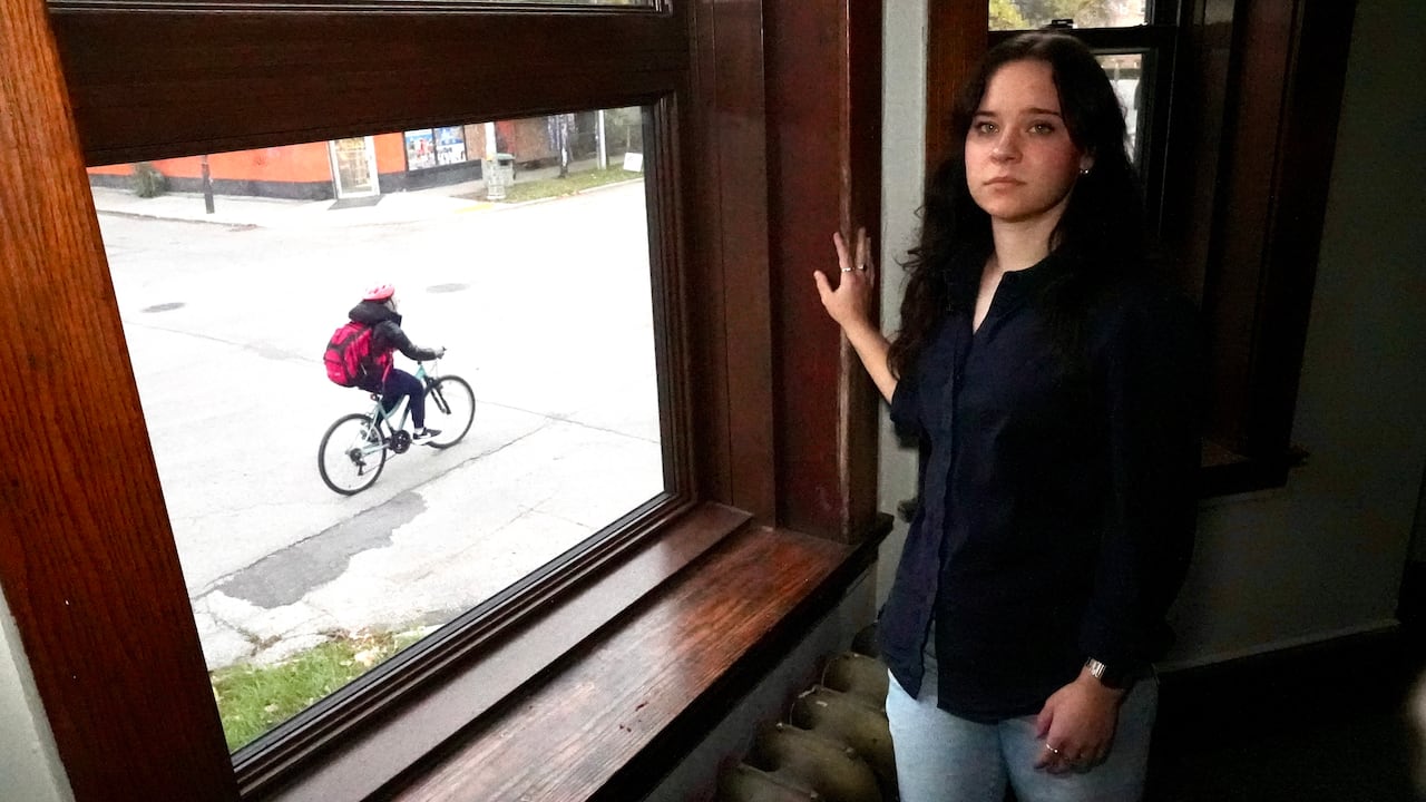 A woman poses by an apartment window as a cyclist passes by.