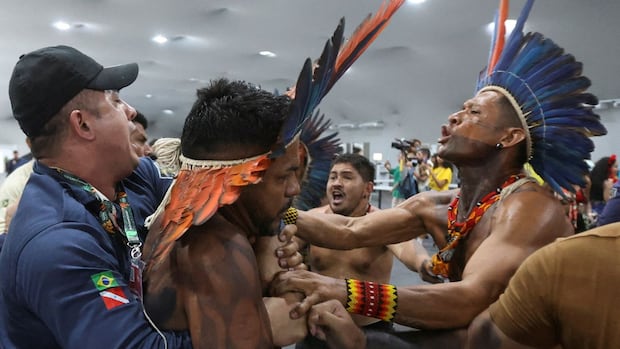 A tense confrontation between men wearing vibrant feathered headdresses and traditional attire. The scene is dynamic, conveying intensity and conflict.