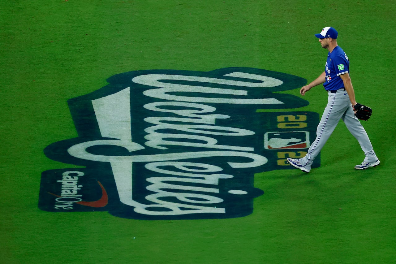 A baseball player walks across the field with the World Series logo painted on the ground.