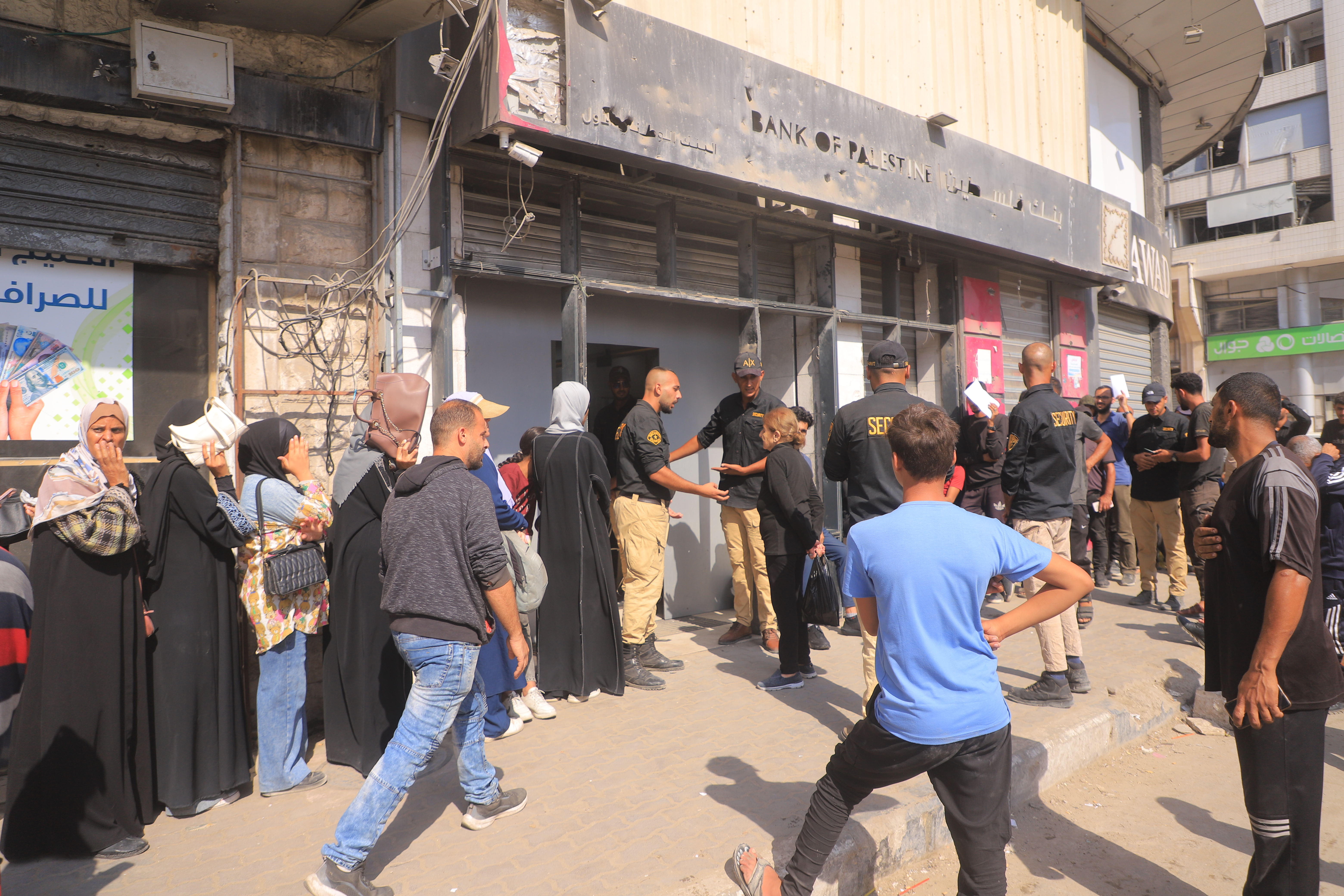 2 bank branches partially reopen in Gaza — without cash; People line up in front of a bank opening\.
