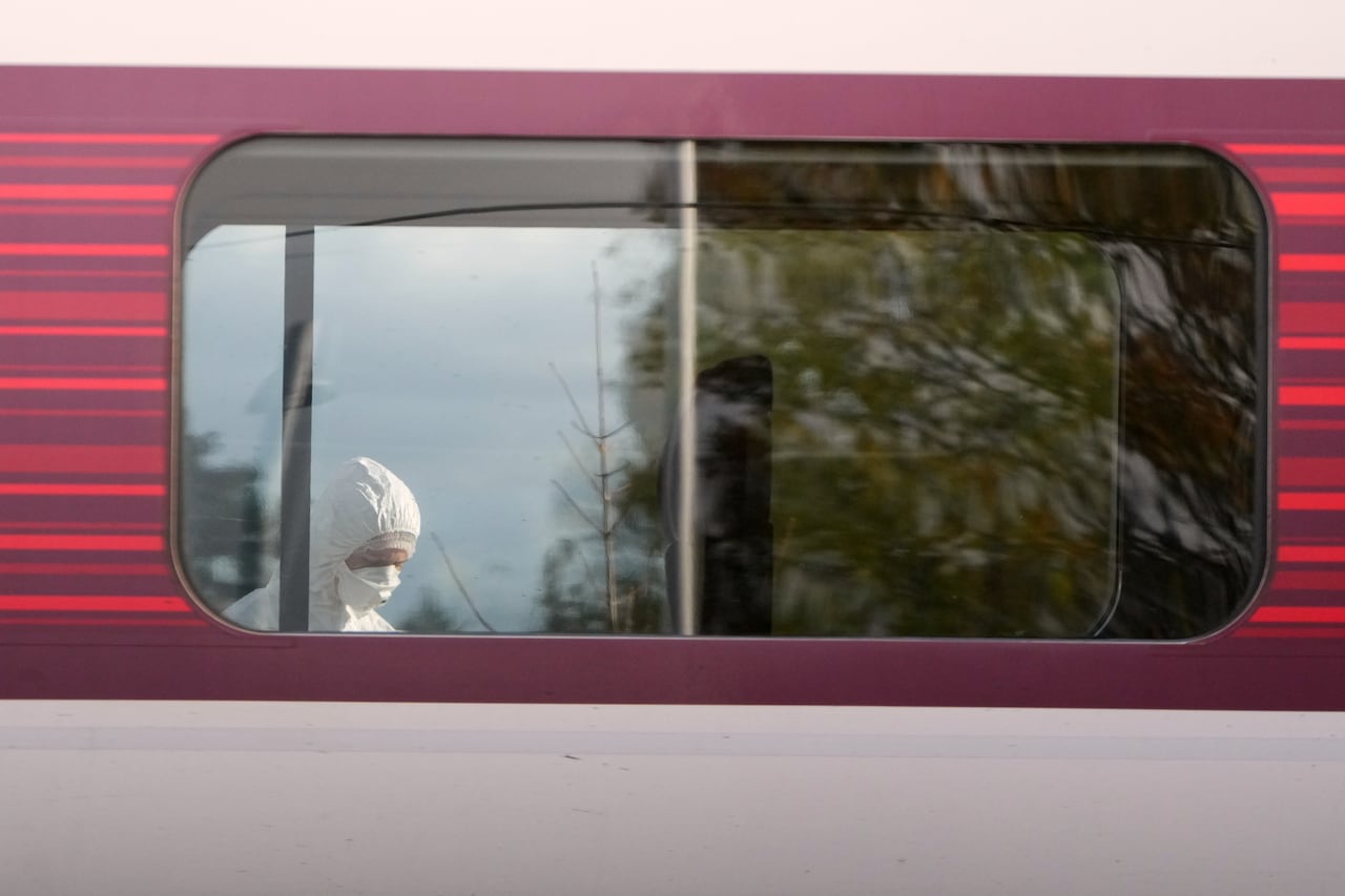A person in personal protective equipment is seen through the window of a train.