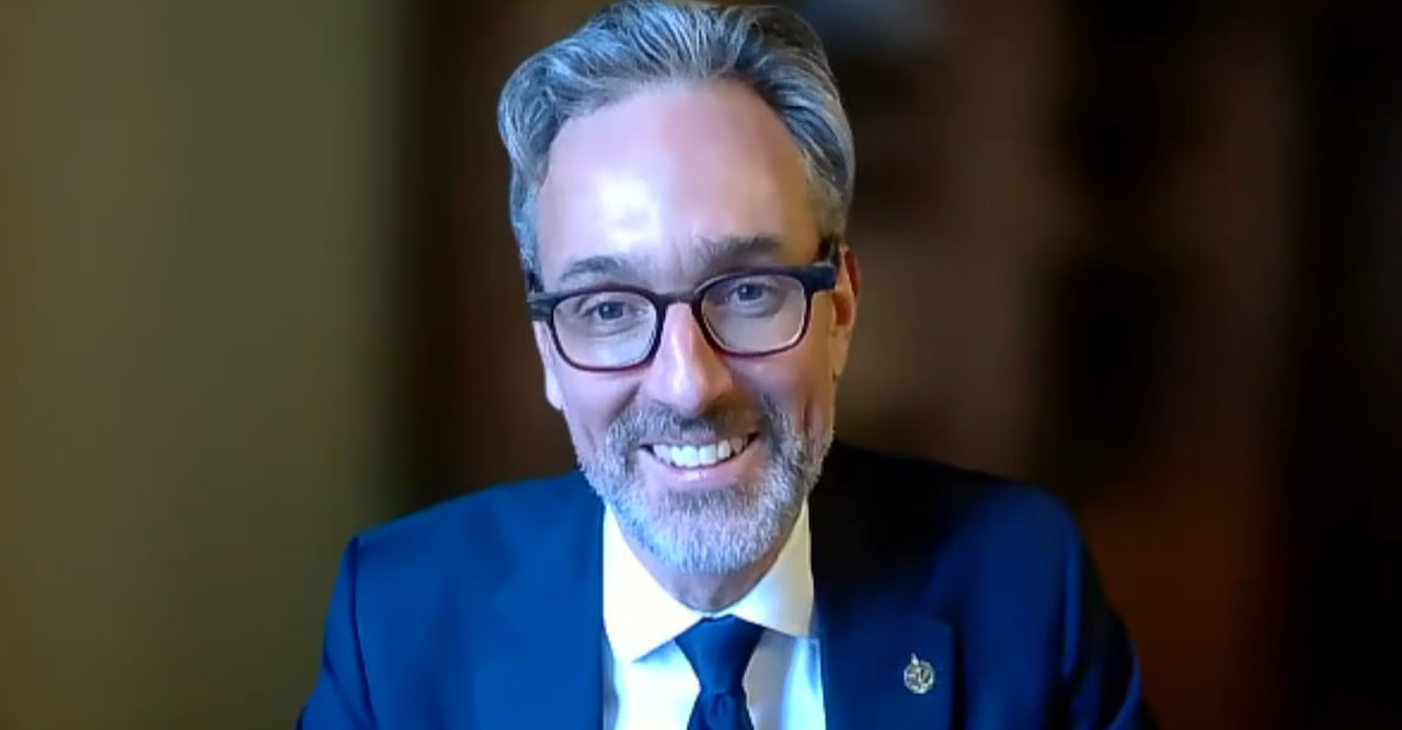 A man with glasses and wearing a navy blue suit, smiles at the camera