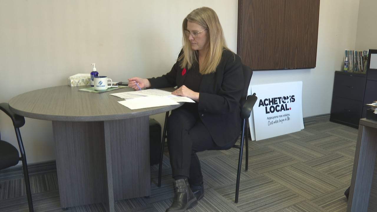 A pistillate sits astatine a table successful an office. She is looking down astatine documents connected the desktop.