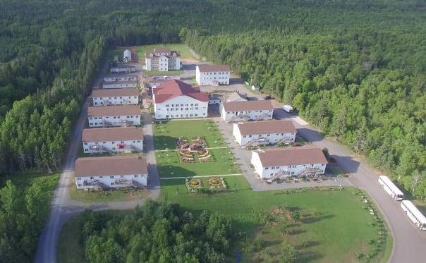 An aerial shot of about 18 buildings on a large plot of grassy land. Most are white with brown roofs.