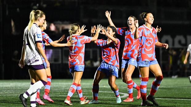 A group of female soccer players celebrate on the field during a game