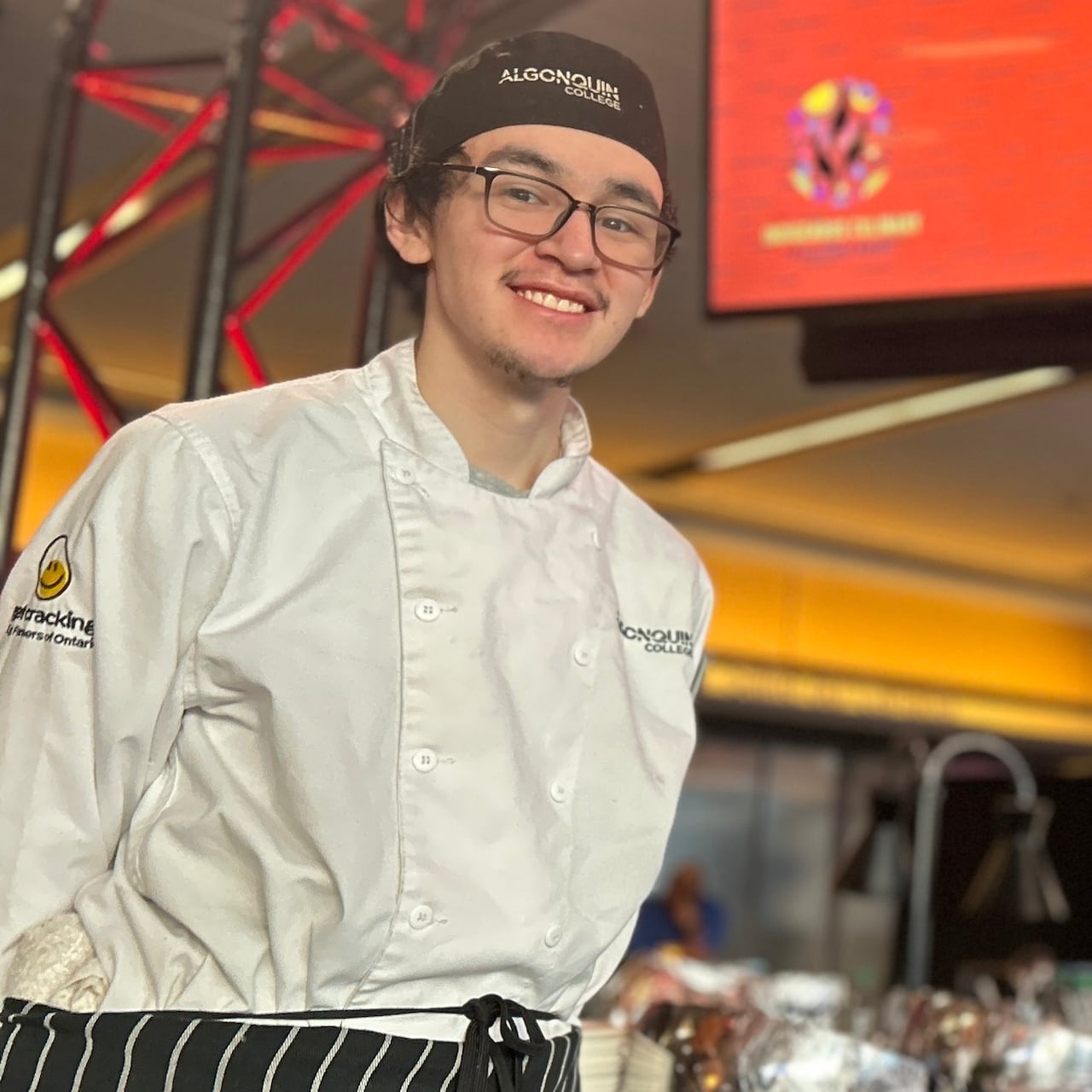 A young Inuk chef poses at an event wearing an apron that reads