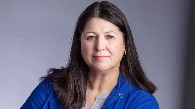 A portrait of a woman with shoulder-length brown hair, wearing a royal blue hoodie and grey shirt.