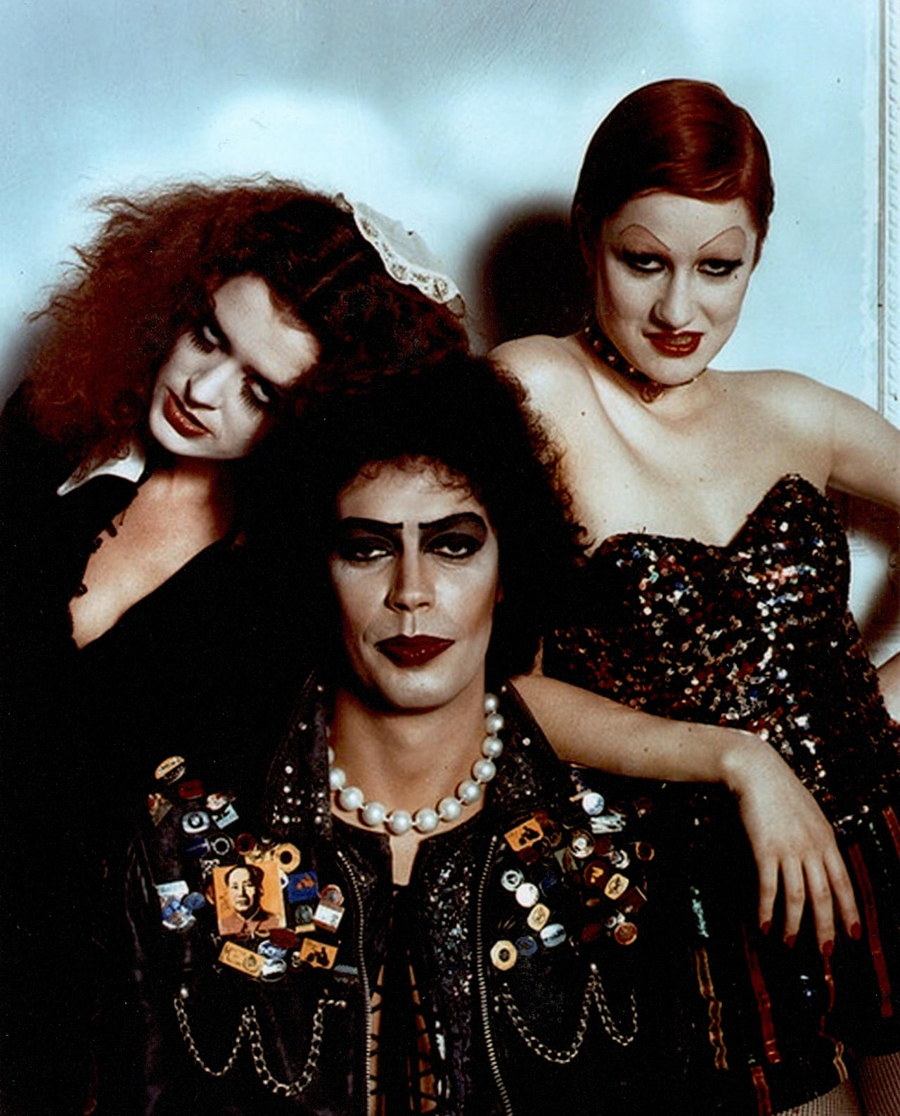Three people with sultry expressions and unique colorful suits look at the camera against a blue background.