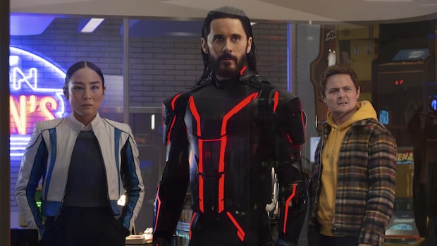 A man wearing a futuristic, lit-up suit stands in front of two confused looking people.