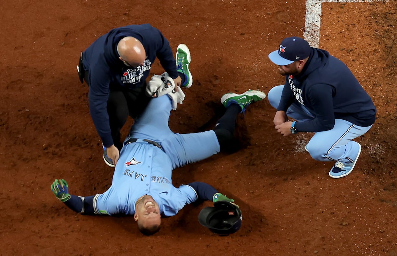A baseball player representing the Toronto Blue Jays lays on the field after getting hit by a pitch.