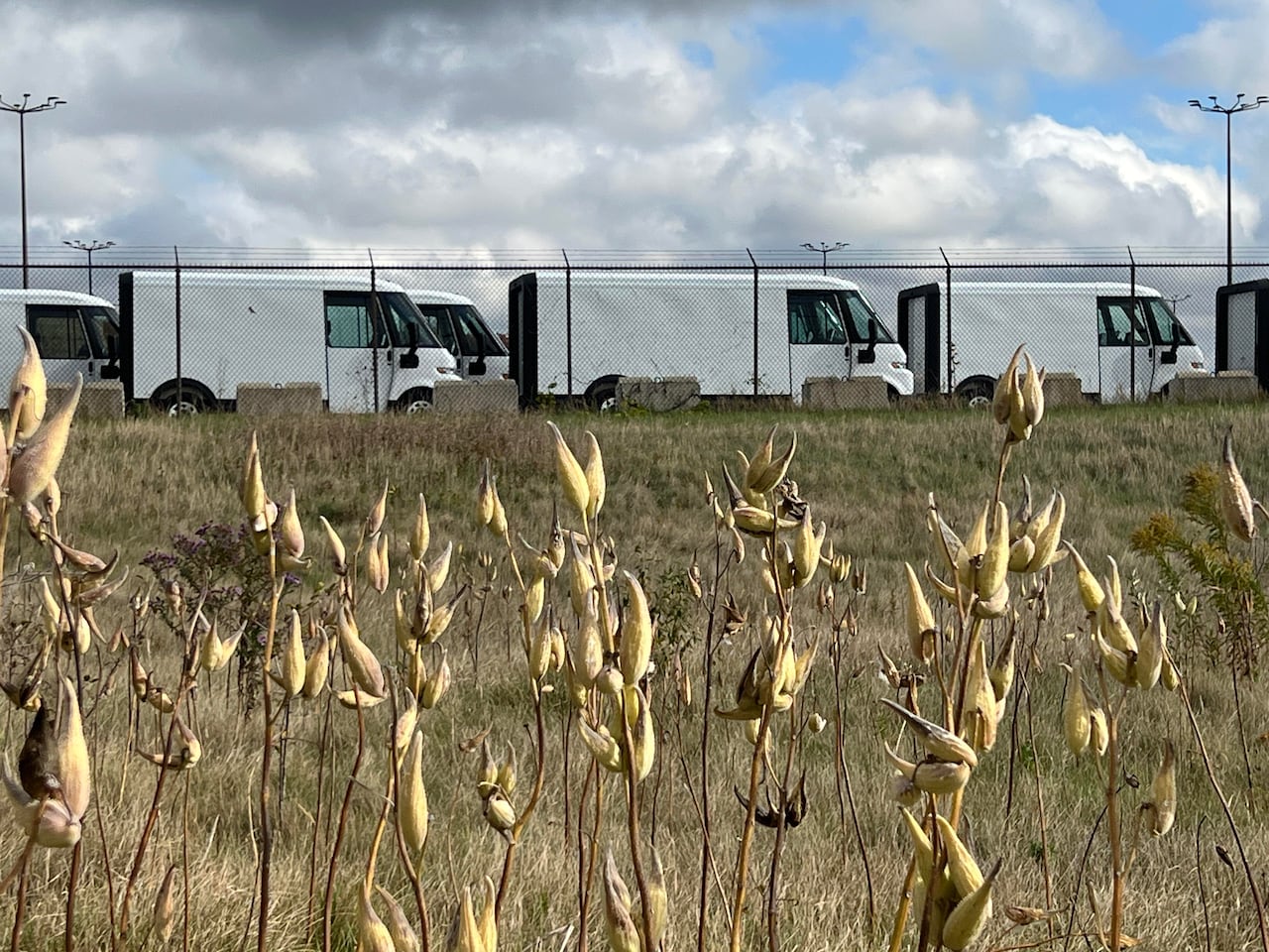 A line of BrightDrop vehicles are parked behind a fenced in parking lot at the GM assembly plant in Ingersoll, Ont.