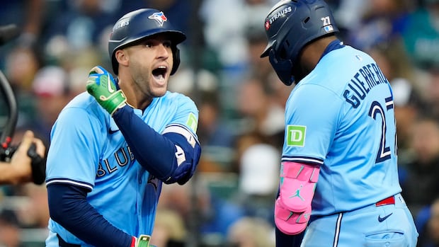 Two baseball players wearing blue uniforms celebrate on the field.