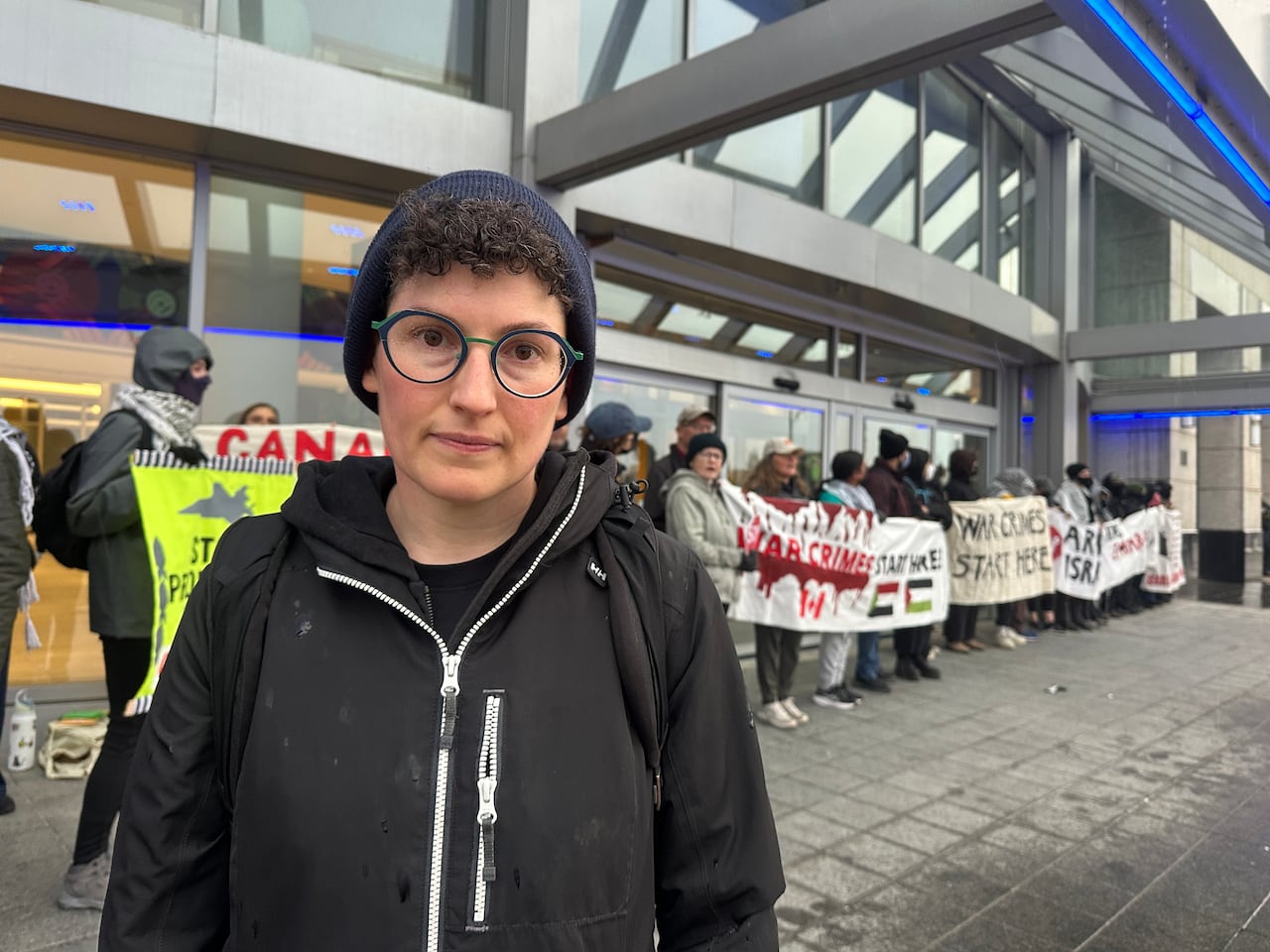Женщина стоит перед шеренгой антивоенных протестующих.