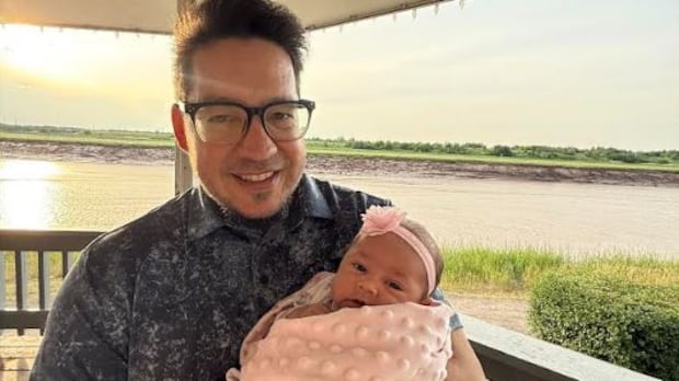 DJ Joseph holding his new granddaughter, Oaklynn, who is the first in his lineage to be ineligible for status.  man holding baby girl in front of sunset