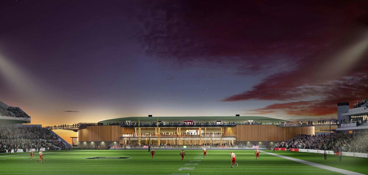 Point of view from the middle of the sports field, looking at a new events centre with a balcony with people standing on it.