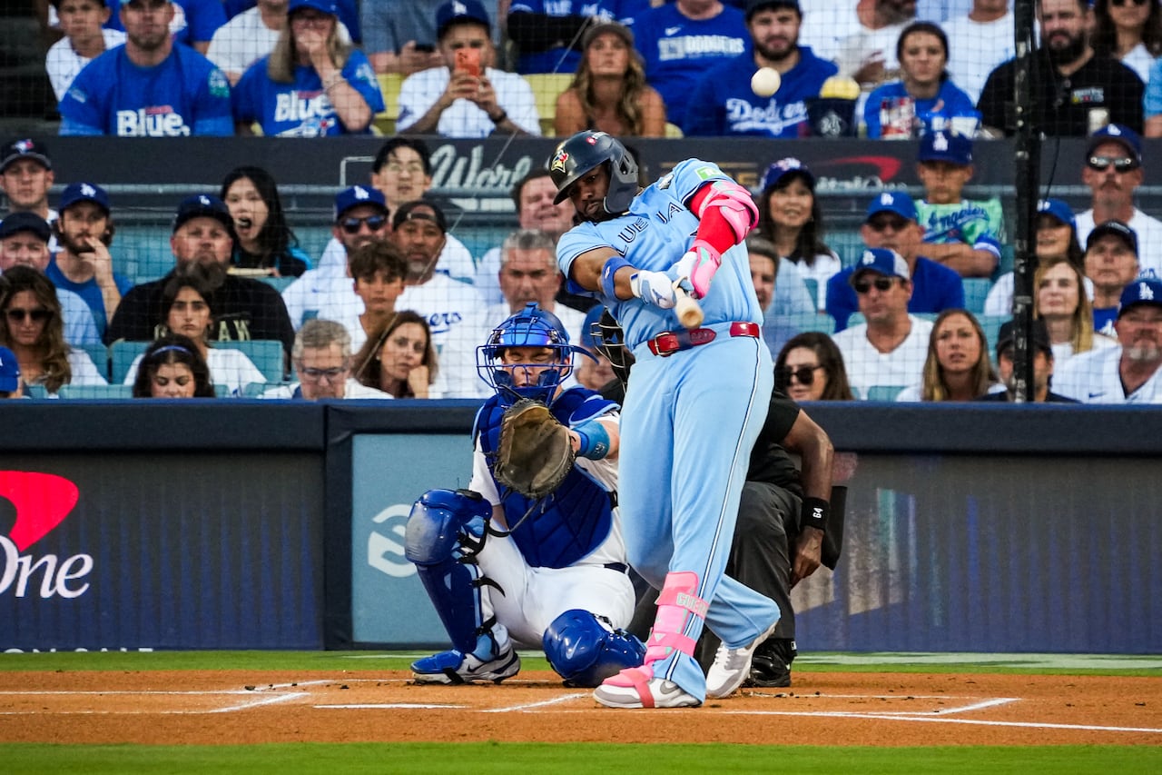 একজন বেসবল খেলোয়াড় বলটি আঘাত করার জন্য একটি ব্যাট সুইং করেন যখন ক্যাচার এবং আম্পায়ার তার পিছনে ক্রুচ করেন এবং ভক্তরা স্ট্যান্ড থেকে দেখেন।