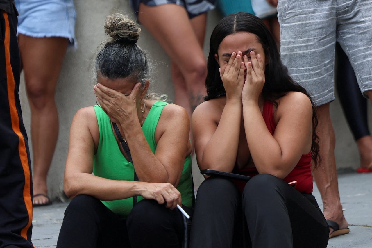 Two women are shown seated and dressed in light clothing, their hands covering their faces in apparent oppression.