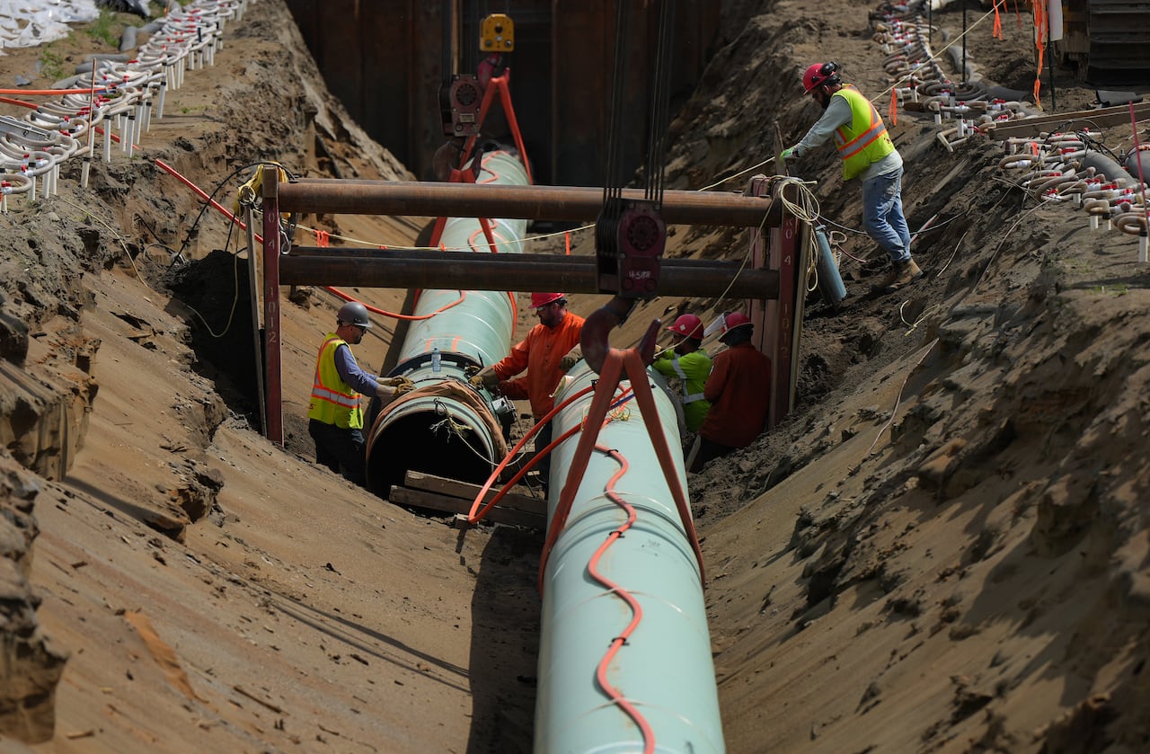 Workers work alongside two large pieces of pipe.
