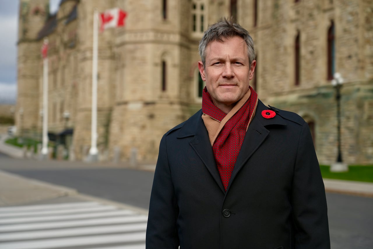 A man in a coat and scarf standing in front of a gothic structure.
