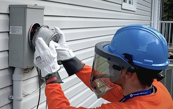 A person in protective equipment and gloves installs a smart meter on the outside of a home.