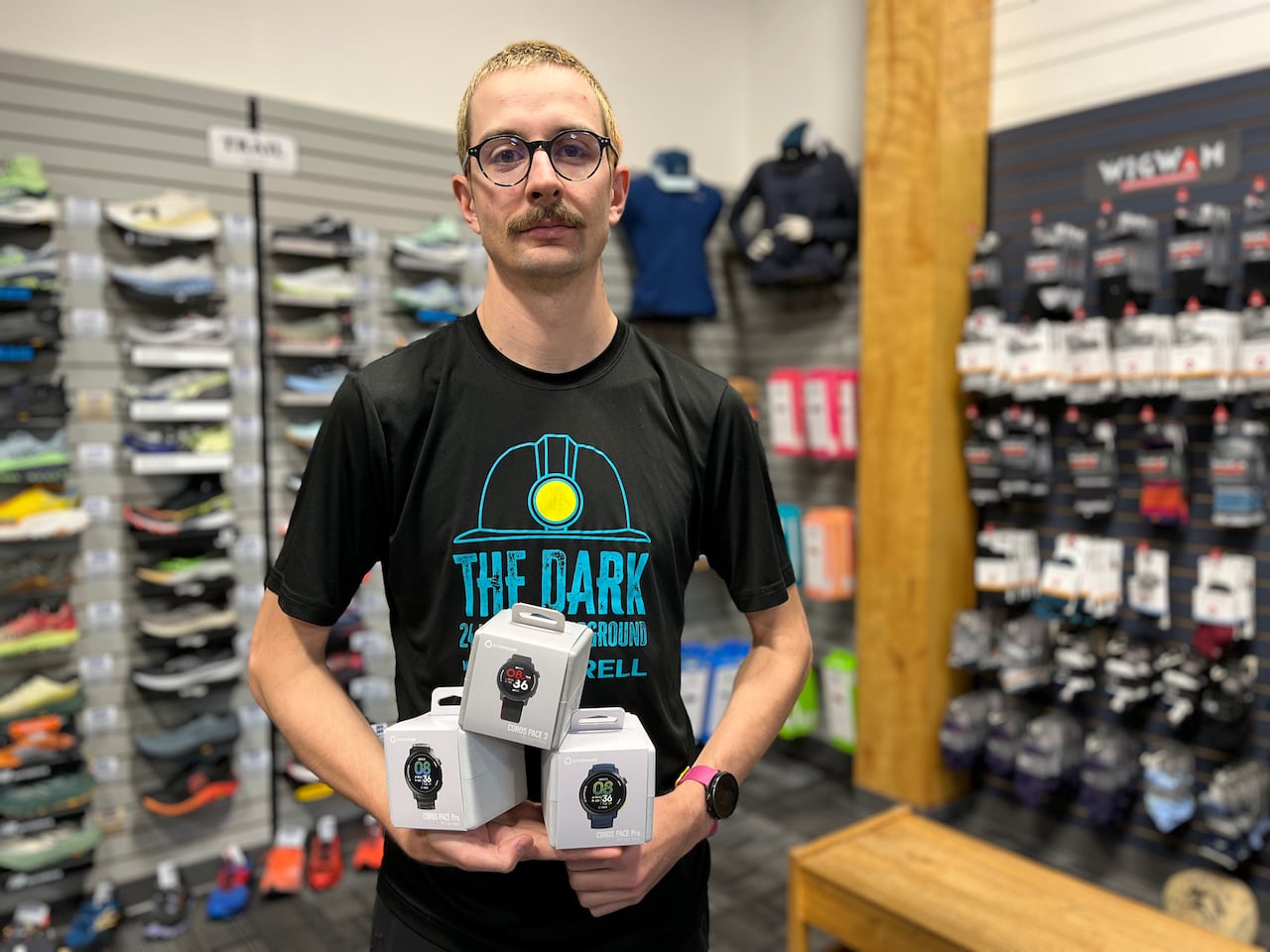 A man in a running store holds three boxes of fitness watches.