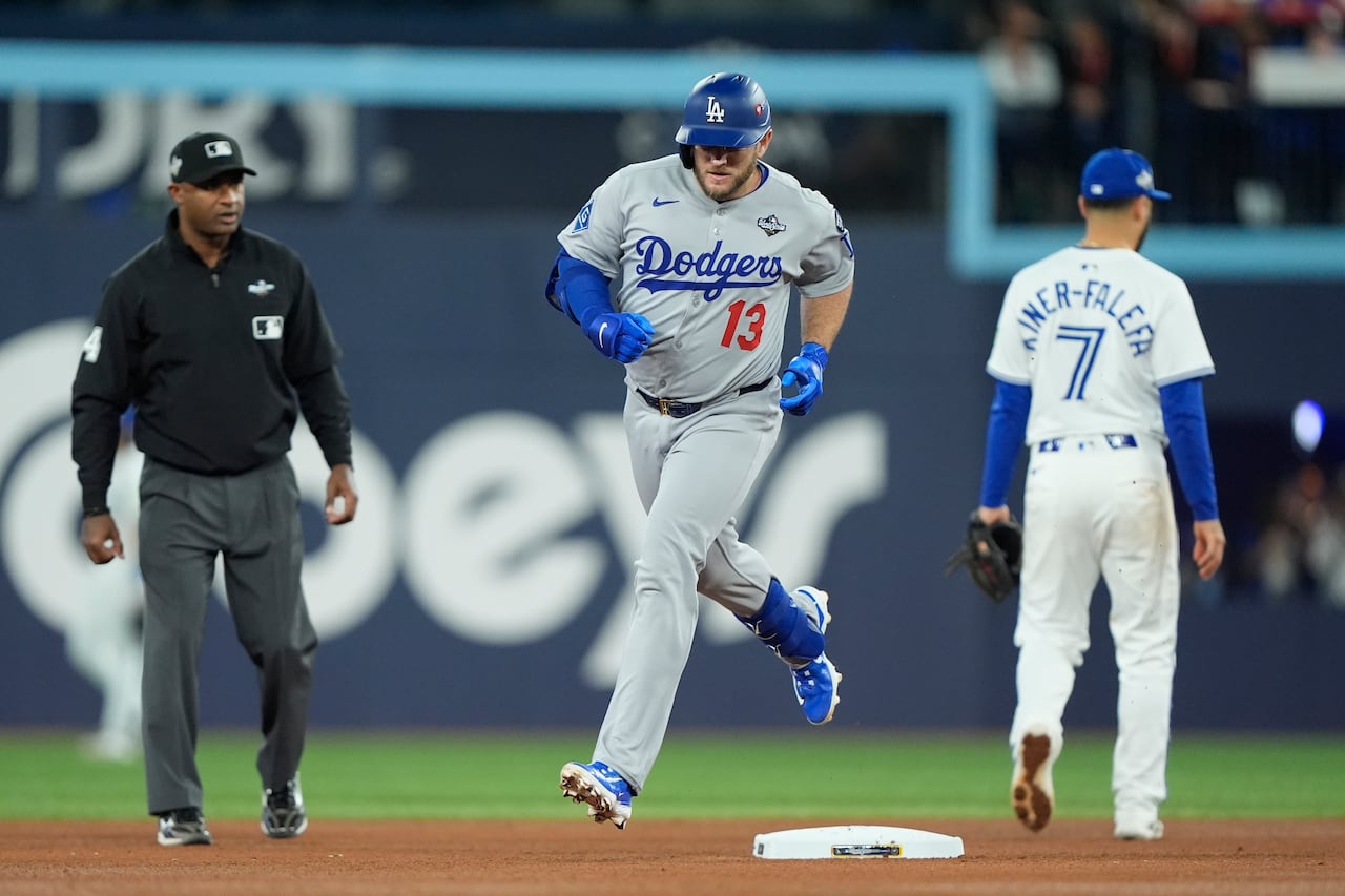 One man runs in a baseball uniform between two other men standing on a baseball field.