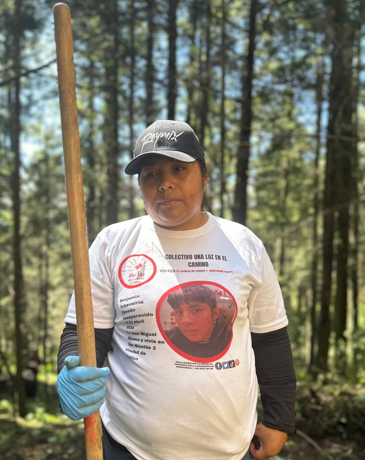 A woman, holding a rake in her right hand, wears the shirt with a photo of her son.