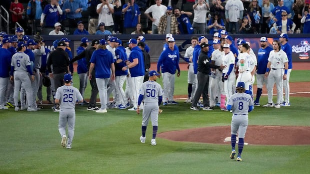 Two large groups of baseball players in a crowd on a field, one team in white uniforms and some with blue hoodies on, and the other team in grey uniforms.