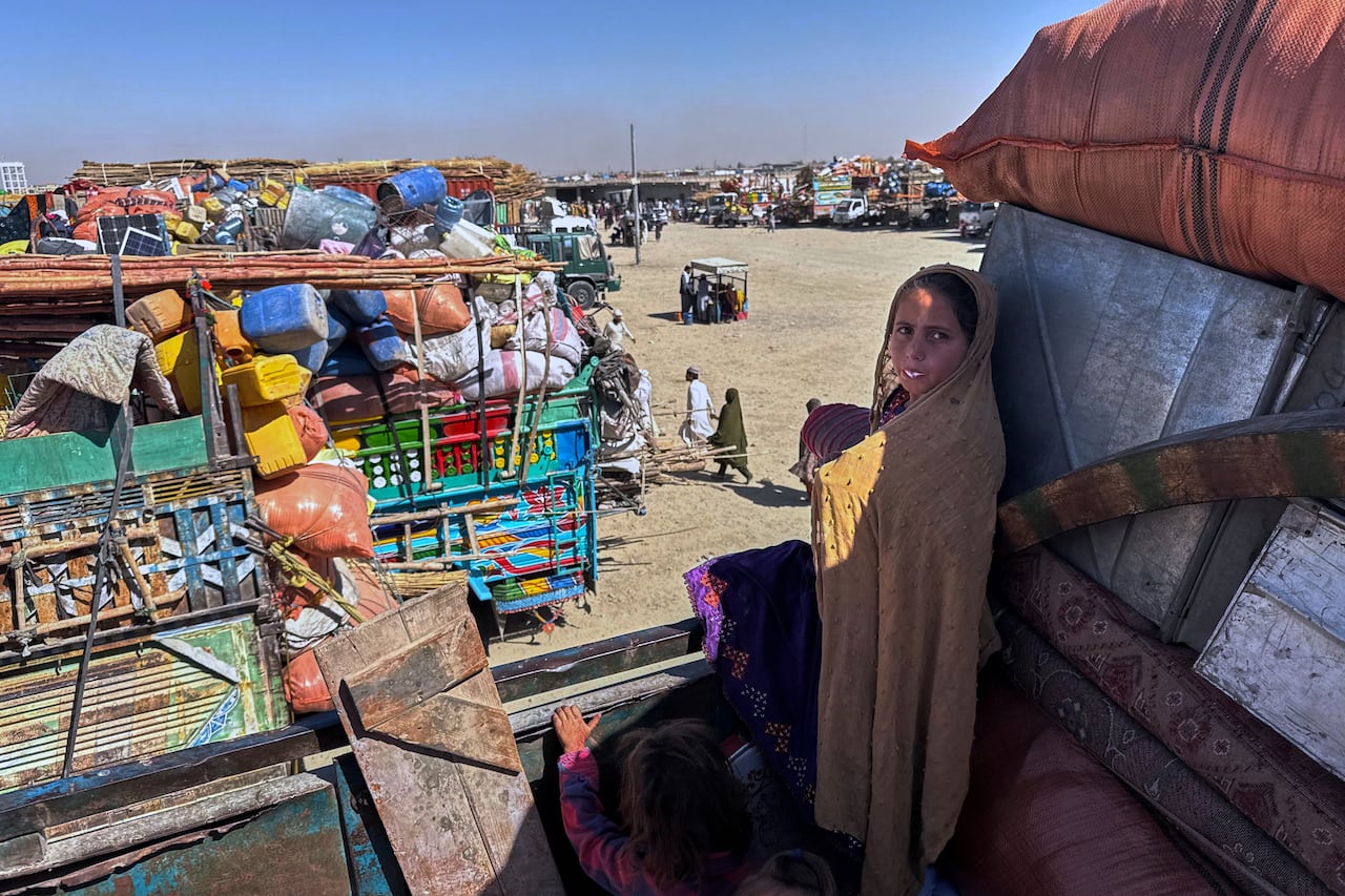 A girl stares into the camera from the bed of a truck in an area with several trucks stacked with property.