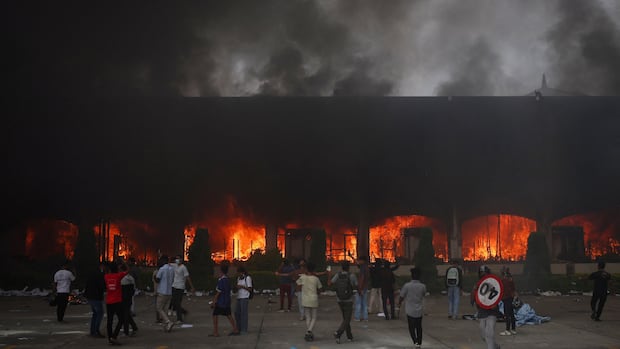 A crowd of people in front of a building on fire with black smoke billowing out of it.