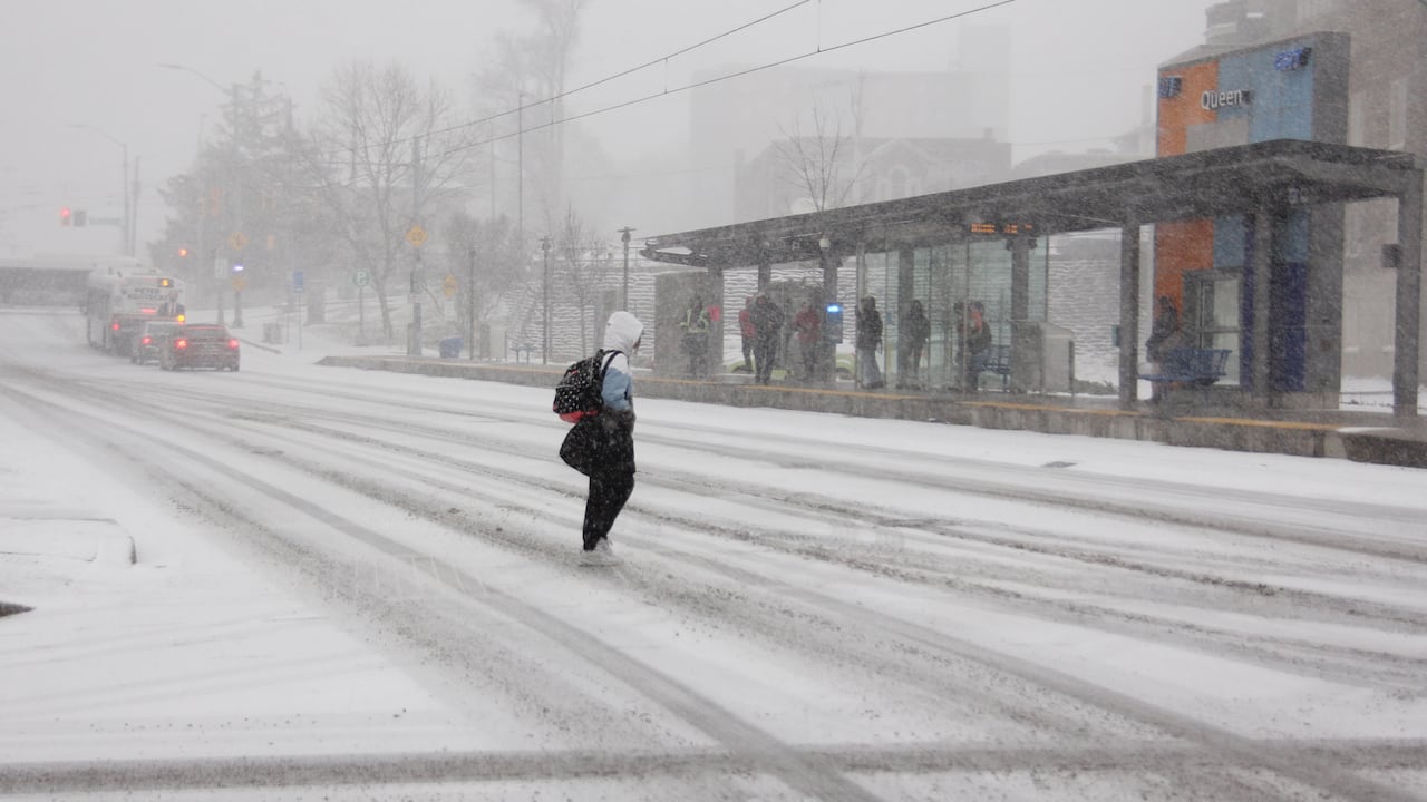 A idiosyncratic   walks a snow-covered intersection adjacent   an LRT presumption    successful  downtown Kitchener