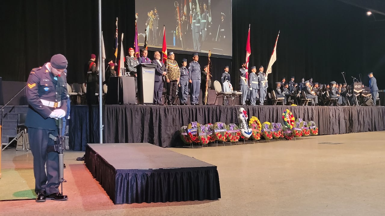 身着制服的士兵站在台上,台前摆放着加拿大国旗和花圈。